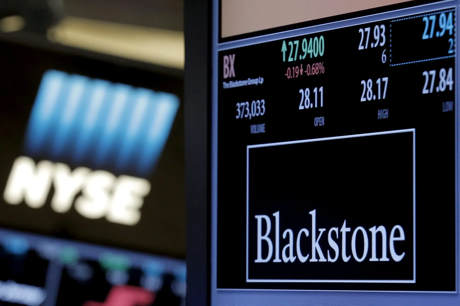 A trading-floor display at the New York Stock Exchange quoting Blackstone (BX), the lit NYSE sign out of focus behind it