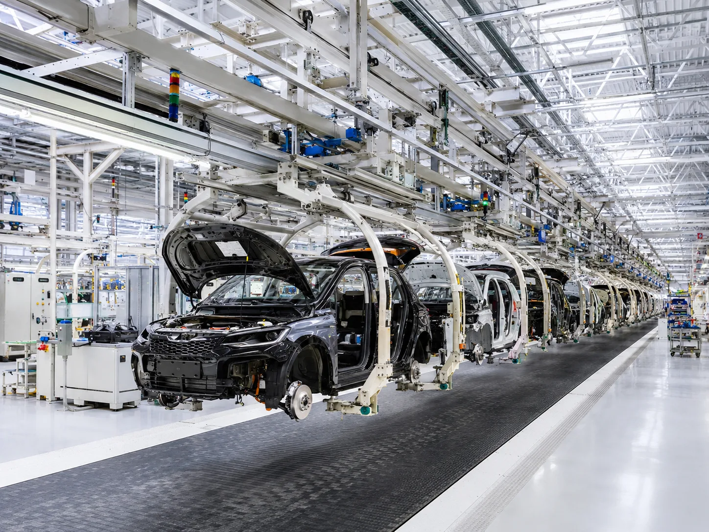 A modern automotive assembly line: car bodies with hoods and tailgates raised, carried down the line on white overhead conveyor frames through a bright plant hall